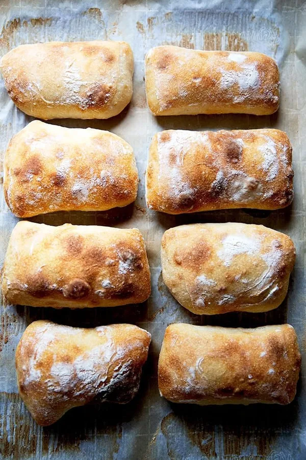 Eight floury sourdough ciabatta rolls on parchment